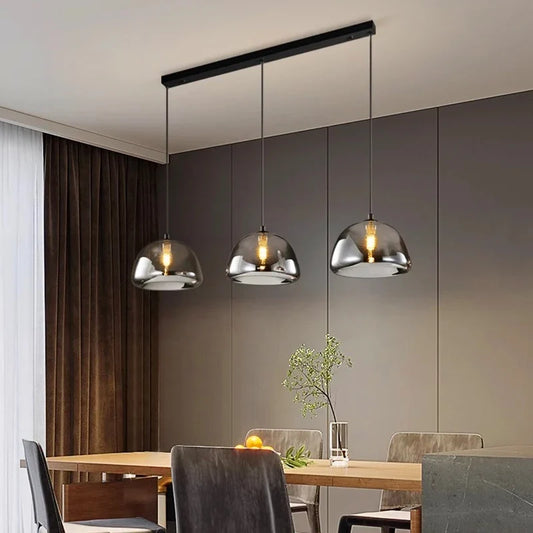 Three pendant lights hanging over a dining table with a vase and fruit on it, in a dining room setting.
