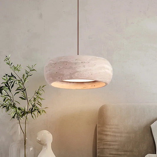 A wabi sabi style pendant light made of travertine hangs from a ceiling with a light inside, casting a warm glow.