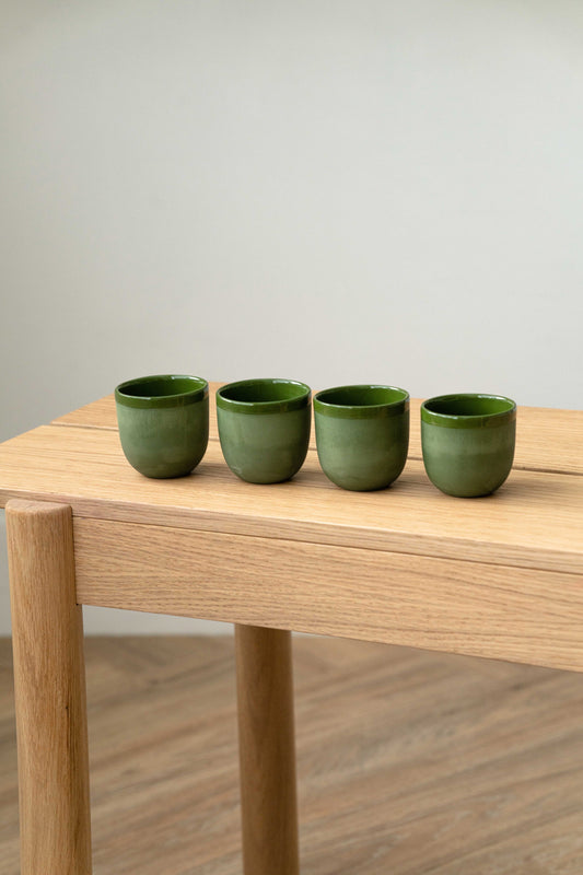 Four vibrant green handmade porcelain espresso cups displayed on a minimalist wooden table.