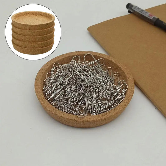 Coaster filled with paperclips on a desk next to a notepad and pen.