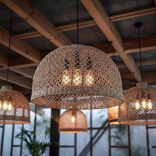 Light fixtures with woven jute mesh hanging from wooden beams under a glass ceiling, lit with warm light, surrounded by plants.
