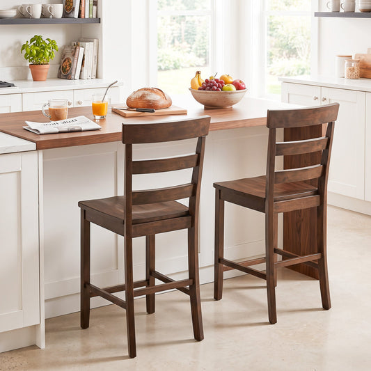 2 wooden counter height bar stools with latticed backs, placed at a wooden kitchen island with fruit and coffee cup on display