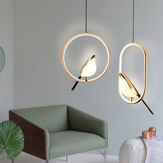 Modern pendant lights with circular frames and stylized bird details, hanging indoors against a grey wall with accompanying furniture.