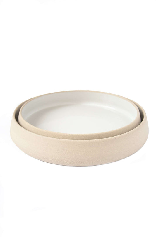 A set of two beige handcrafted stoneware dinner plates with a white interior, stacked together