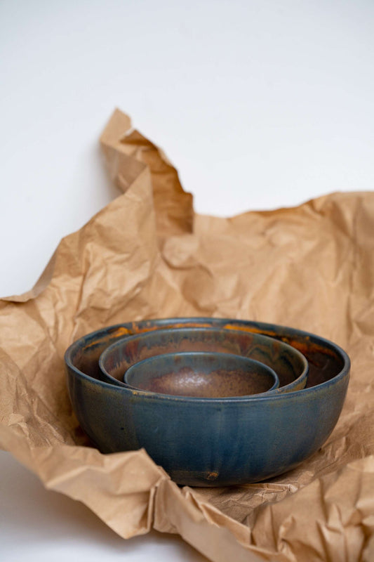 Nested blue-handled bowls atop brown crumpled paper on white background.