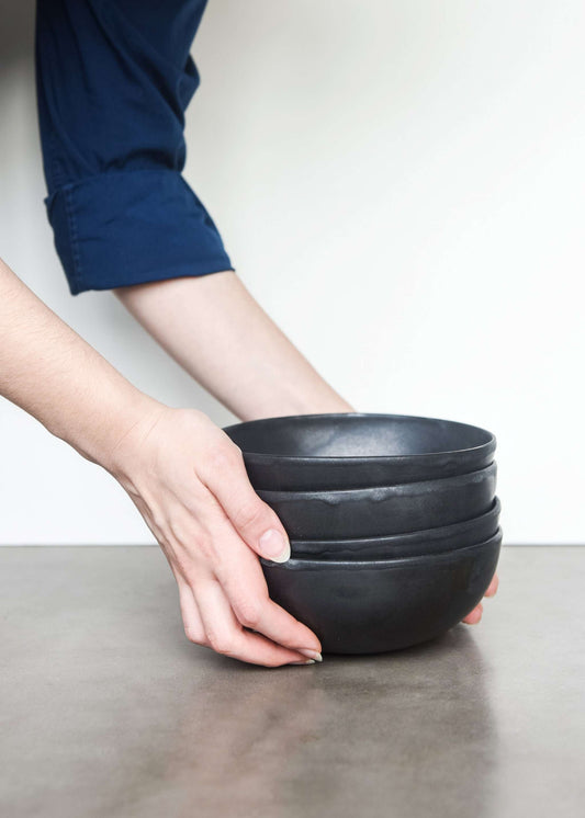 Hands holding stacked bowls, black matte, stoneware, modern interior setting