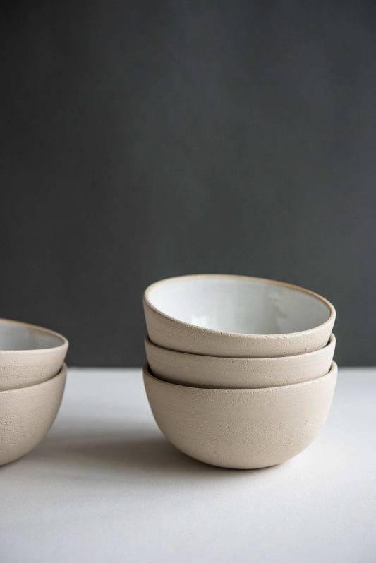 Stack of handmade stoneware bowls with a beige glaze, set against a dark gray background.