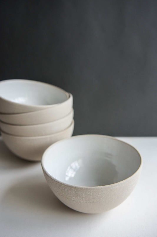 Beige handmade stoneware soup bowl on white surface with more bowls stacked in the background.