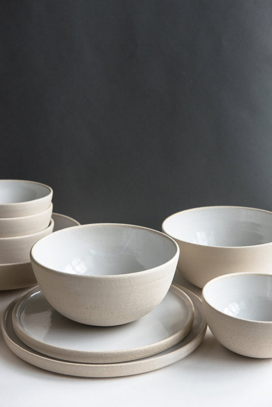 Stacked stoneware bowls and plates in light gray on a white surface against a dark background.