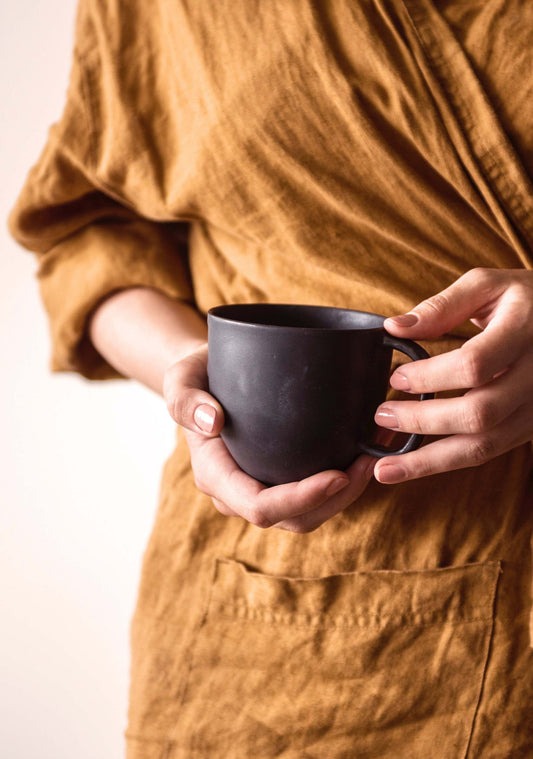 Person in mustard dress holding matte black coffee mug.