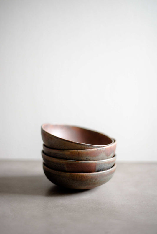Stack of rustic stoneware mini bowls with earthy tones on a neutral surface