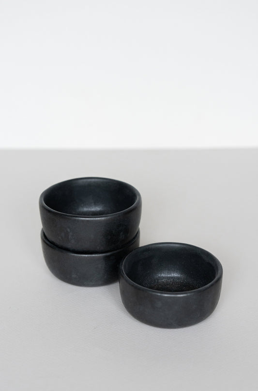 Stack of three matte black stoneware pinch bowls on a plain white surface.