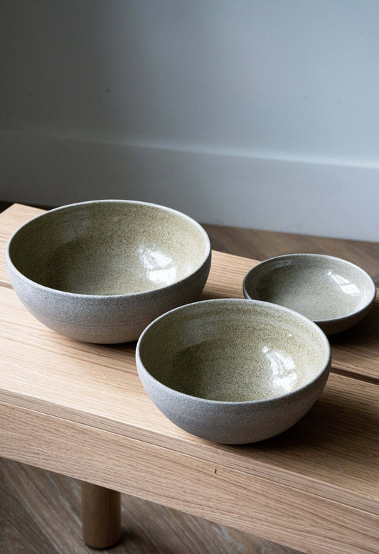 Three textured concrete bowls of varying sizes on a light wooden shelf, simple background.