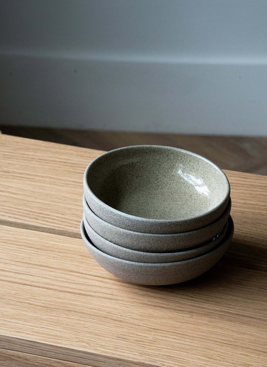 Four grey speckled stoneware bowls stacked on a light wooden surface.