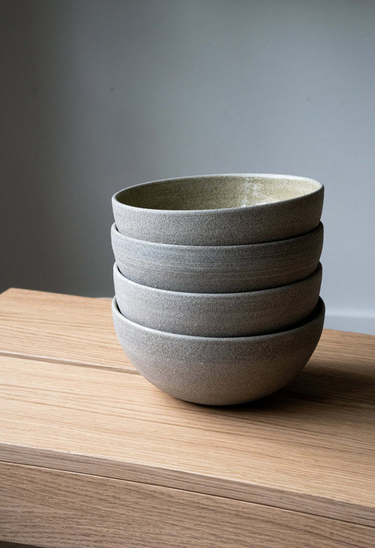 Stack of five textured ceramic bowls on a wooden surface with a plain background