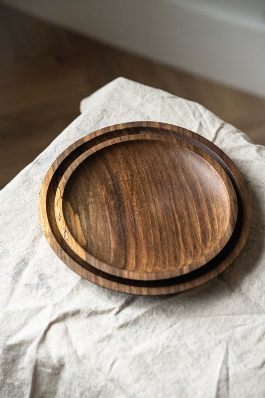Two round, hand-carved wooden plates on a beige cloth on a wooden floor.