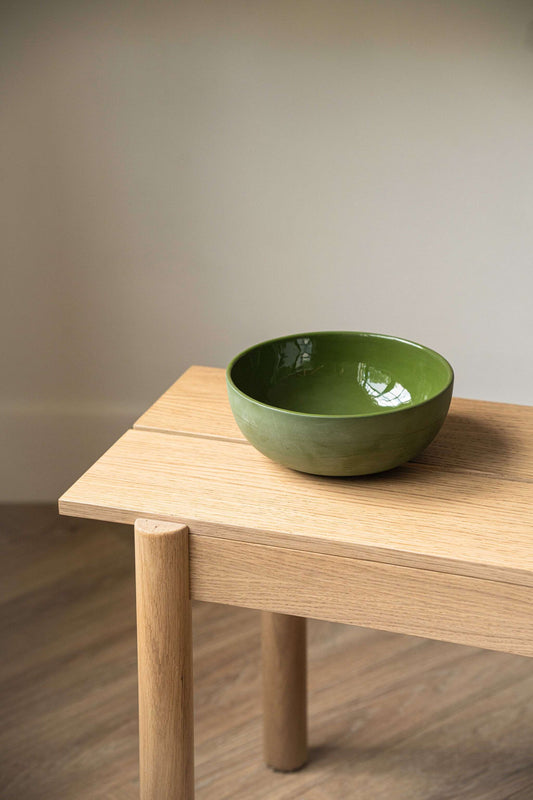 A light green handmade porcelain salad bowl sits on a wooden table against a neutral background.