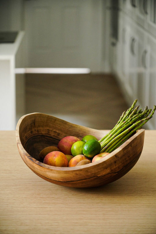 Handcrafted wooden bowl filled with fresh fruits and asparagus on a table.