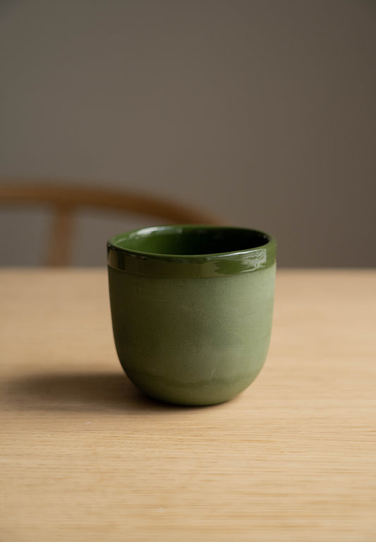 A matte green handmade porcelain coffee cup on a wooden surface.