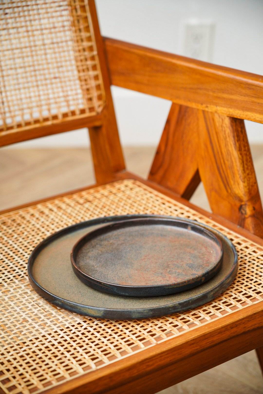 Rustic stoneware plate with a subtle greenish hue and a glossy matte finish, placed on a wooden cane chair.