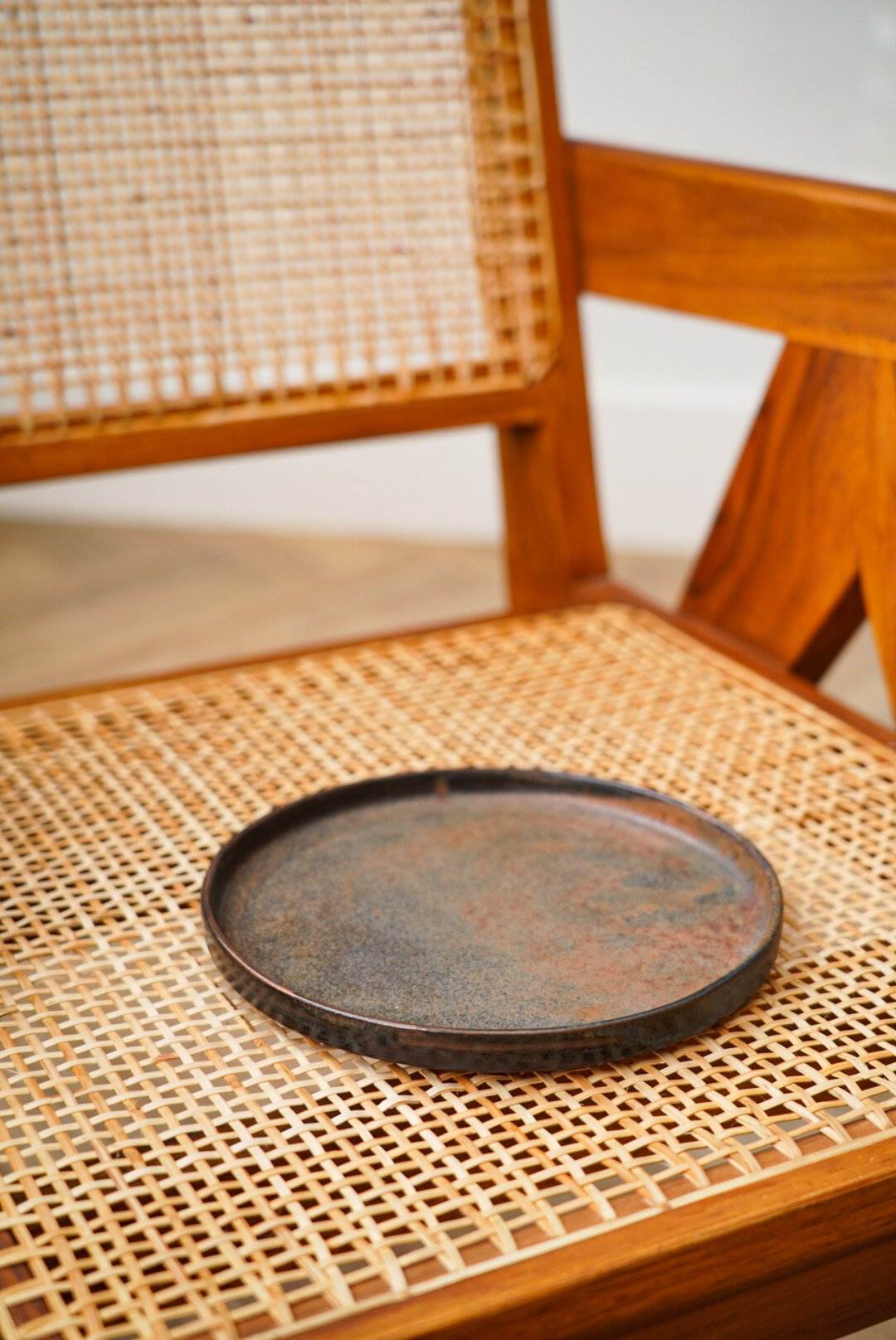 A Stoneware Rust Dinner Plate on a woven chair seat.