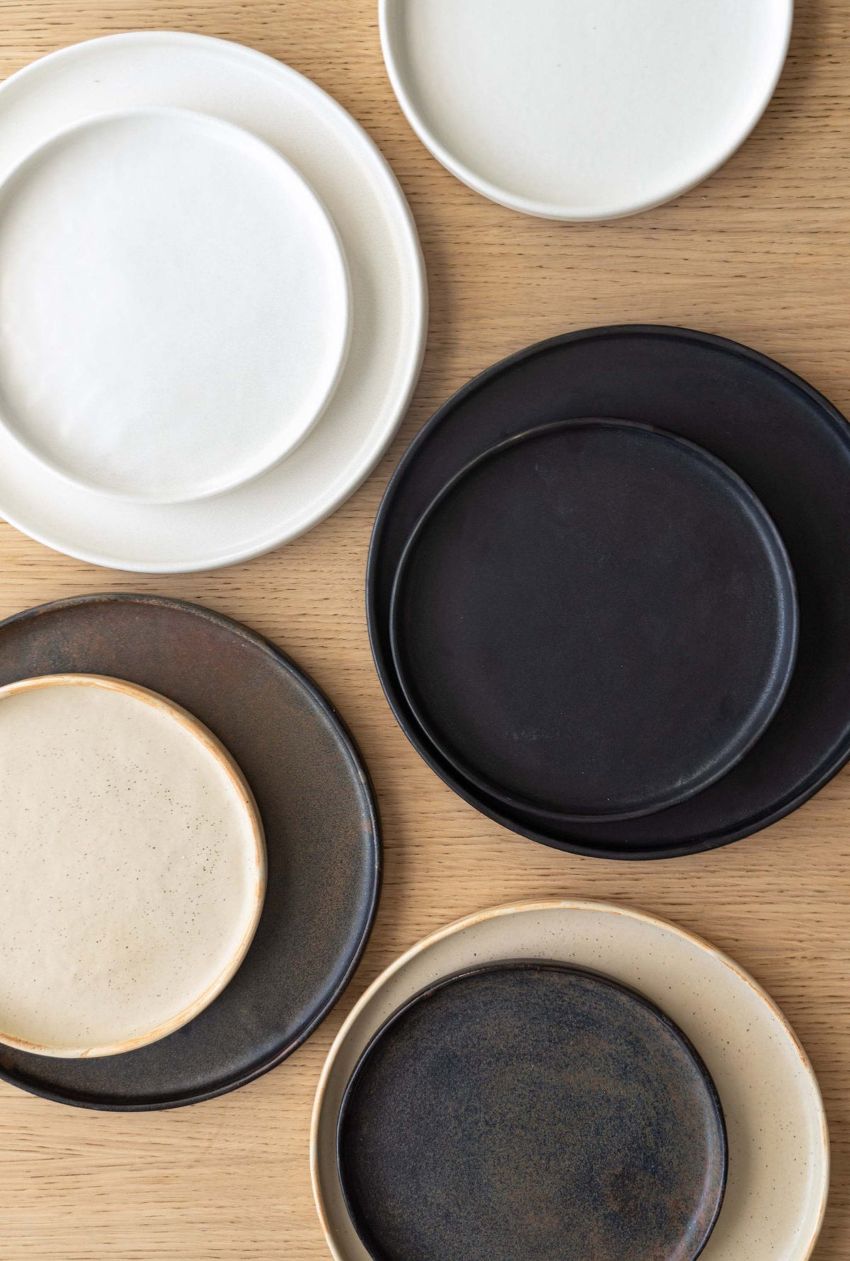 Stoneware rust dinner plates with a worn, textured finish in muted beige and black tones displayed on a light brown wooden surface.