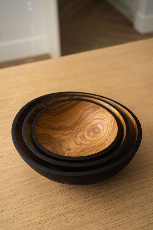 Stack of dark brown charred ashwood nesting bowls on a light wood table