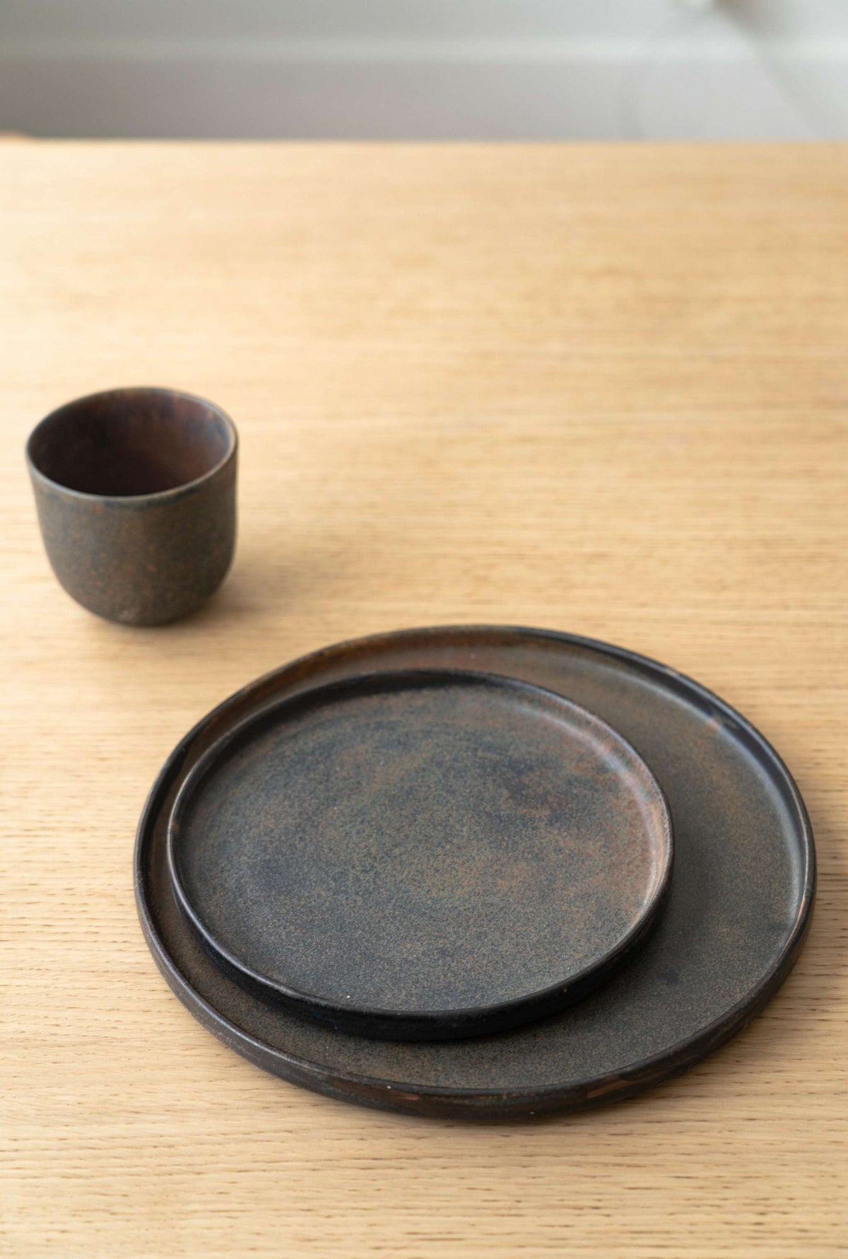 Two dark brown Stoneware Rust Dinner Plates on a light wooden table, minimalistic design