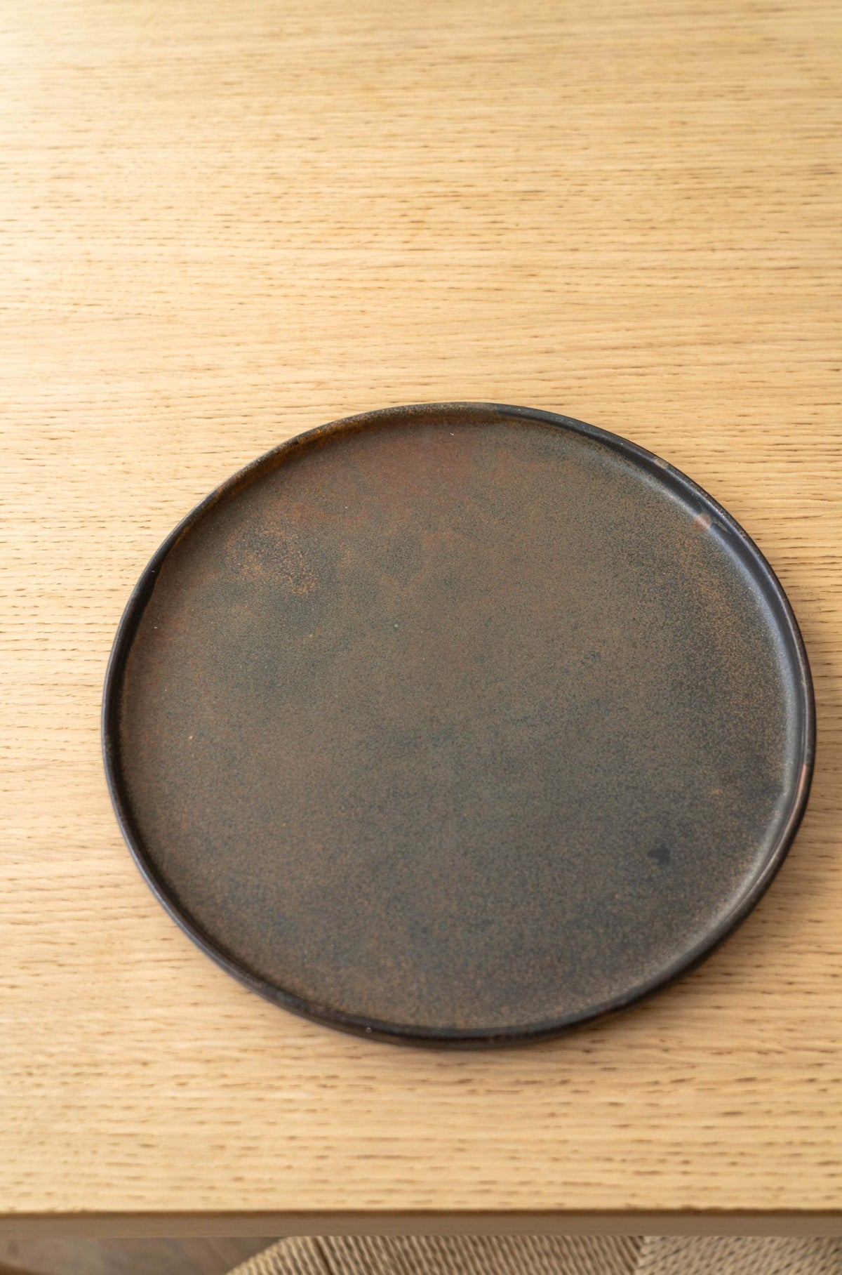 Rustic, dark stoneware dinner plate with subtle textured finish on light wood surface