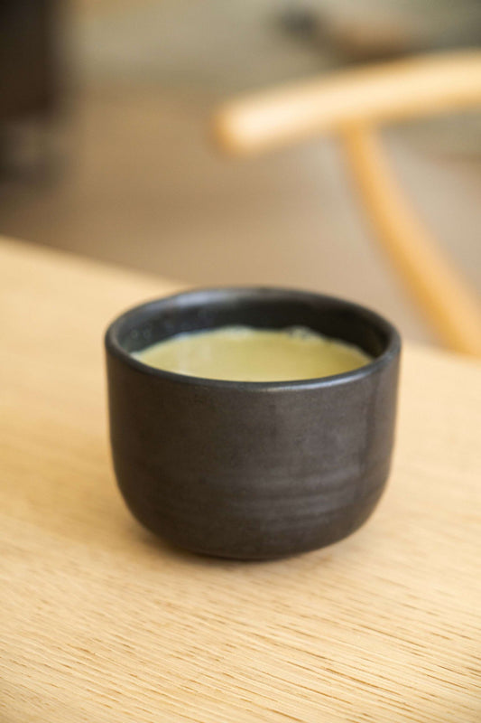 Stoneware black bowl with yellow liquid inside, placed on wooden surface