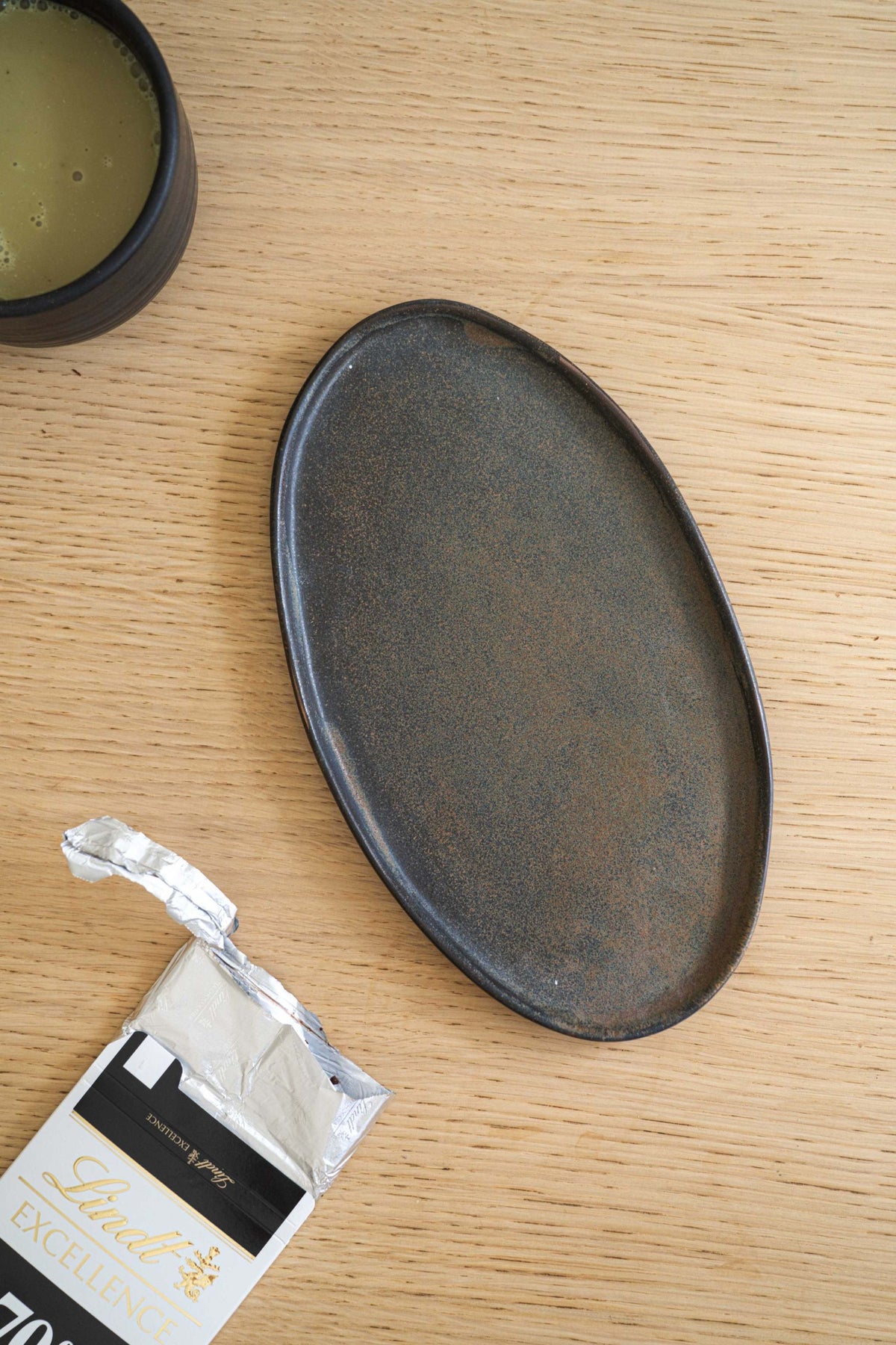 Rustic oval serving platter, matte finish, dark brown, on wooden table.