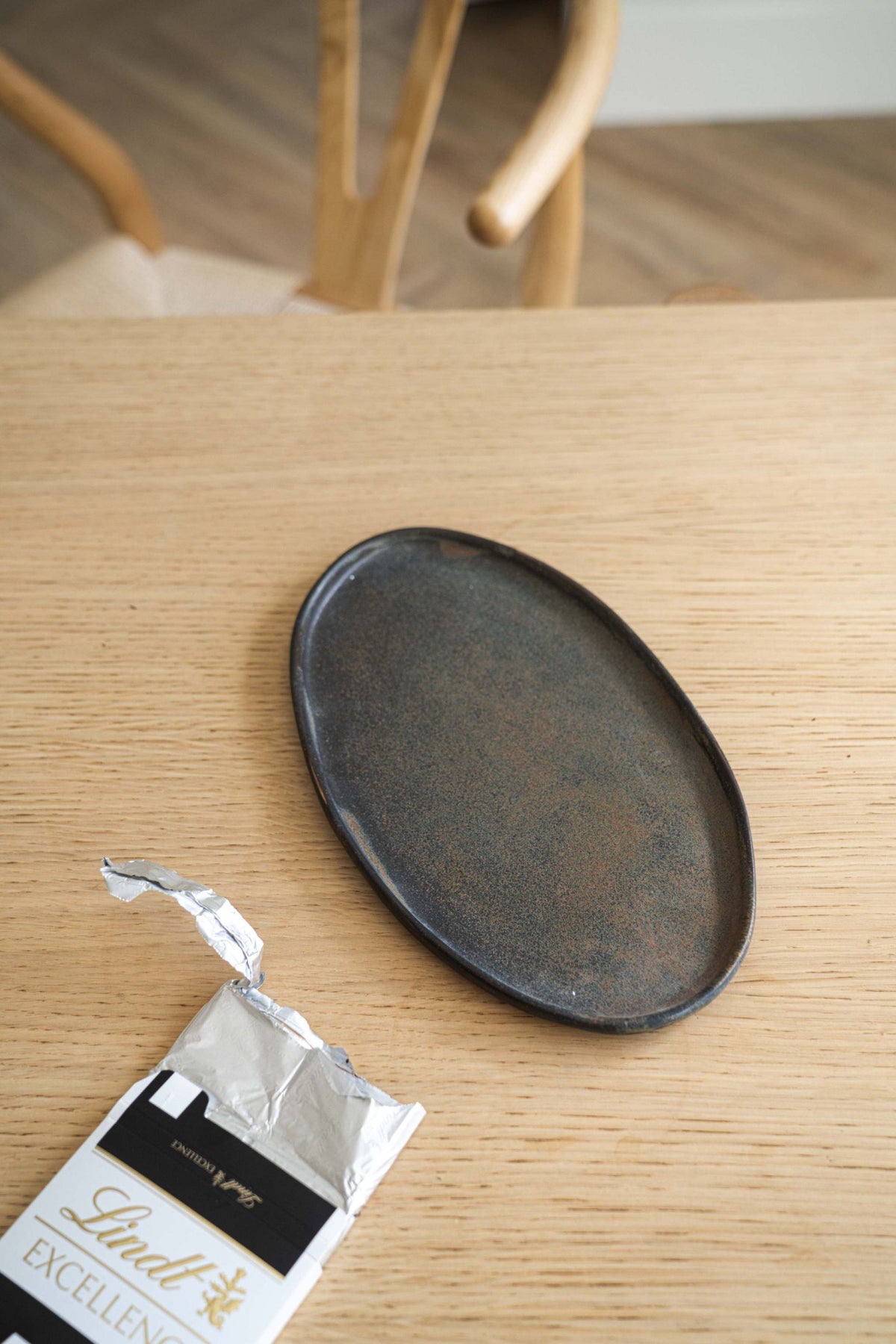 Oval dark matte serving platter on light wood table with Lindt chocolate wrapper