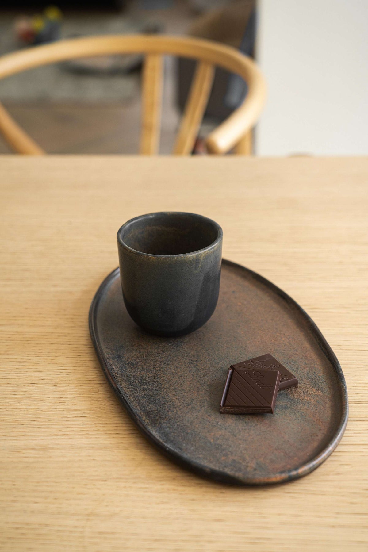 Rust matte stoneware serving platter with dark chocolate bar and cup, displayed on wooden table.