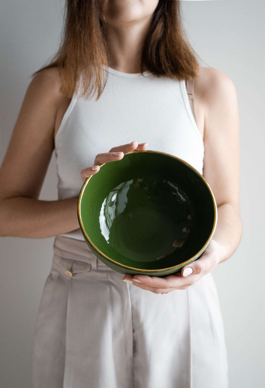 A woman holds a glossy green salade bowl with a gold rim.