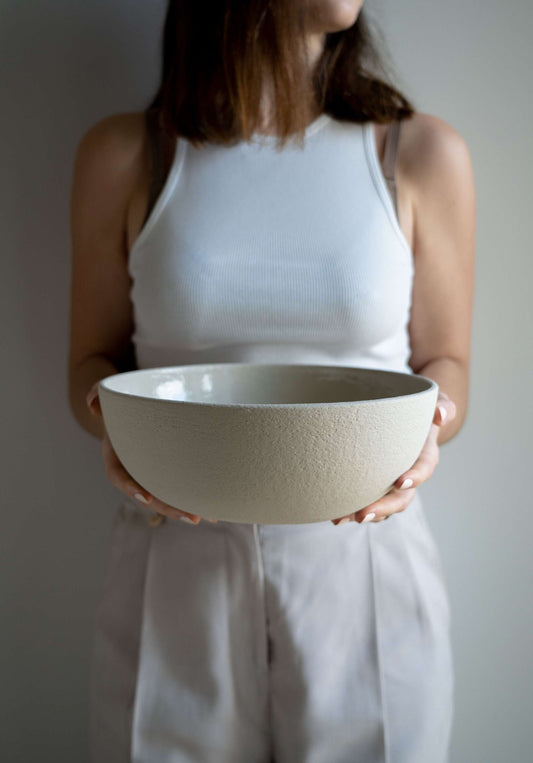 Person holding a large stoneware fruit bowl with a textured finish and transparent glaze.