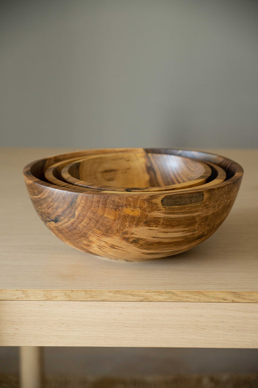 Nested wooden bowls with distinct grain patterns on a light wooden shelf