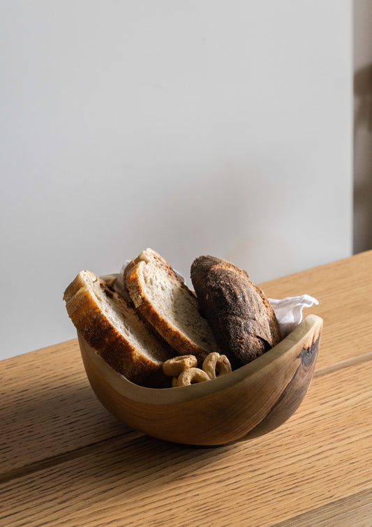 Wooden bowl with bread and cashews, resting on wooden surface.