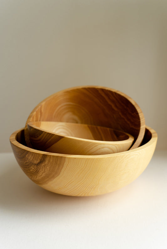 Three nested wooden bowls with visible wood grain and a natural finish, arranged on a plain surface.