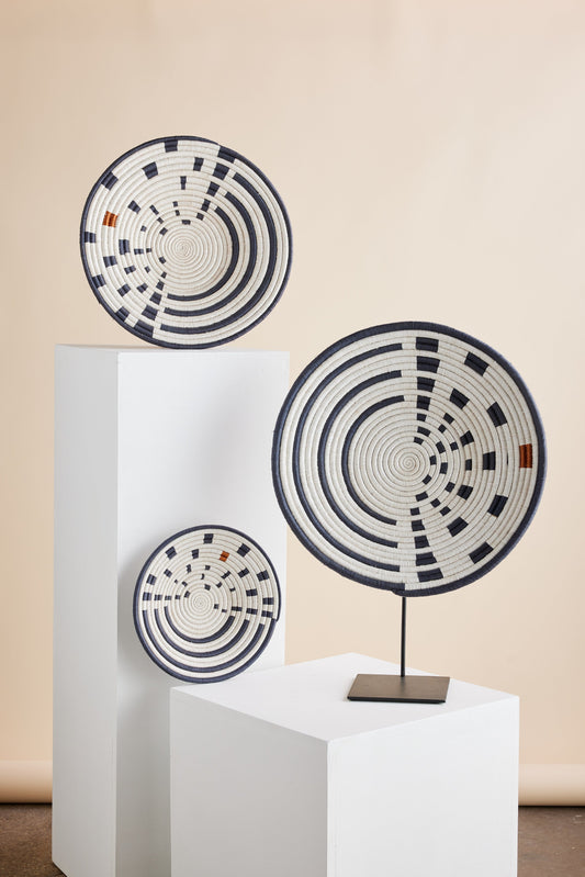 Three Sunrise Wall Baskets, made of natural fiber with geometric patterns, displayed on white stands against a beige wall.