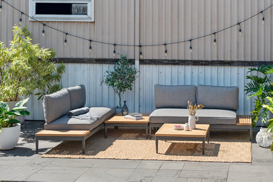 Outdoor seating set with gray cushions and wooden accents on a patio with plants and string lights.