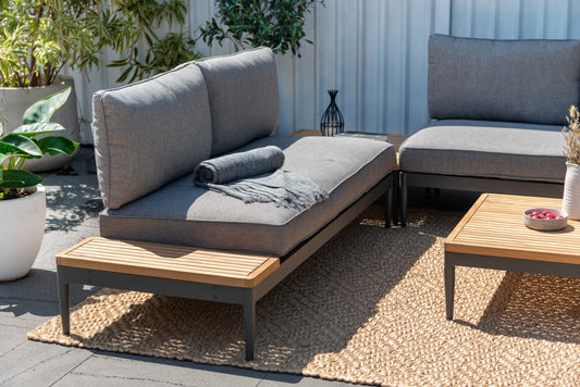 Modern 2-seater sofa with cushion and blanket, teak and metal table, jute rug, plants, wooden fence background
