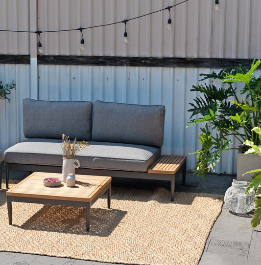 Outdoor seating set with wooden and fabric components on a rug, gray cushions.