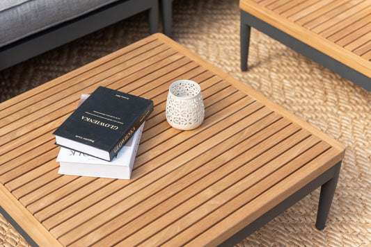 Stack of books and white perforated cup on wooden slatted coffee table in modern living room setting.
