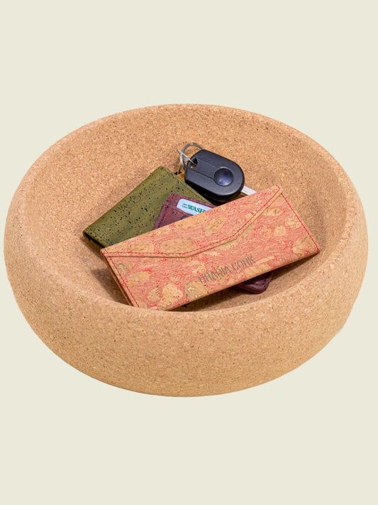 Cork bowl holding small items like a key fob and folded wallets, natural cork texture.
