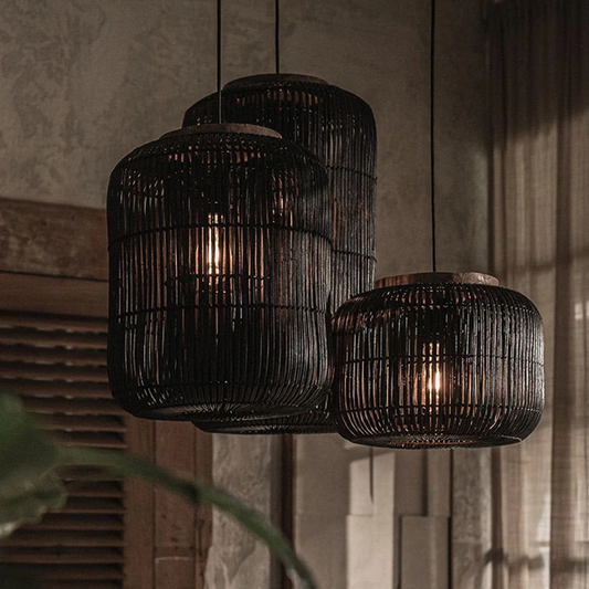 Black rattan lantern chandelier with three hanging cylindrical shades on wooden panels backdrop