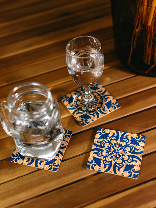 Three biodegradable cork coasters with blue floral patterns supporting glassware on a wooden table.