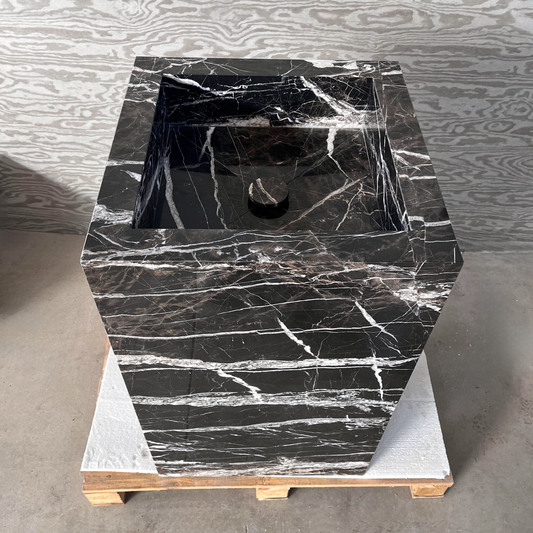 A black marble pedestal sink with white veining on a wooden pallet in a warehouse setting