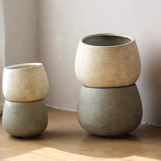 Two rustic cement planters in beige and gray, with a textured finish, stacked in a minimalist setting.