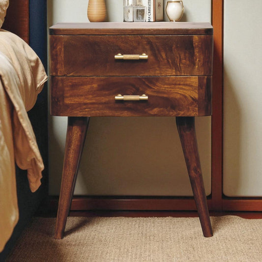 Dark wood nightstand with brass handles, placed against a wall with a beige carpet and part of a bed visible.