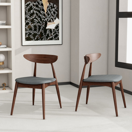 Set of 2 dark brown rubberwood chairs with light gray cushions in a modern interior with a painting and shelves in the background